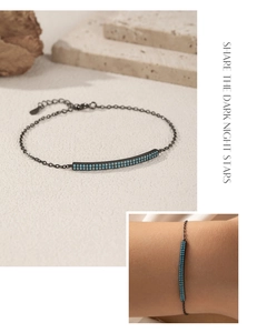 Detail of black chain bracelet with turquoise beads and curved bar on stone background