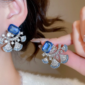 Close-up of luxury silver earrings with blue crystal and square fan-shaped details