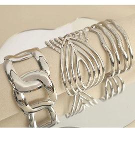 Detail view of silver metal bracelet set featuring chain and heart patterns on a beige display