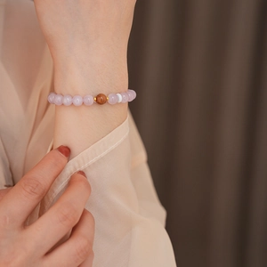Macro view of beaded bracelet with lavender stones, wood accent, and golden spacer beads