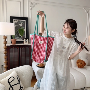Close-up of red and white checkered tote bag with green handles in a French home setting