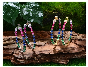Close-up of S925 silver hoop earrings with vibrant colorful teardrop gemstones on moss