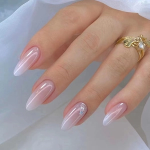 Detail of almond-shaped pink gradient nails with glitter and a gold heart love ring