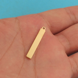 Polished gold stainless steel rectangular bar pendant held in hand for size reference