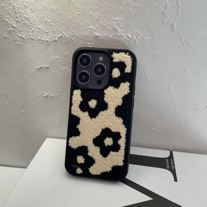 Detail view of plush black and white floral phone case for iPhone Pro on white books