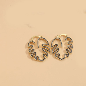 Detail of gold leaf earrings with dark blue zircon inlay on a beige background