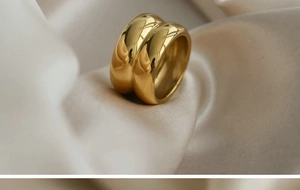 Close-up of golden double-layer wide band ring resting on soft beige silk fabric