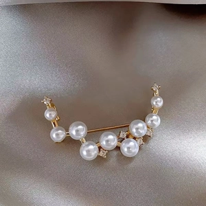 Close-up of elegant gold brooch featuring white pearls and sparkling crystals on silk