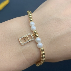 Detailed shot of a gold-beaded bracelet with a hollow diamond heart pendant on a wrist