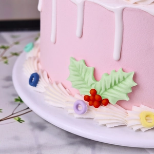 Pink fondant cake decorated with green holly leaves and red berries for Christmas baking