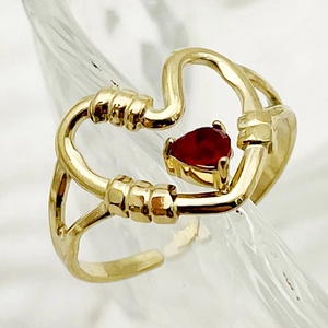 Detailed view of a gold plated heart ring with a red gemstone on a glass edge