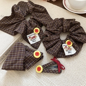 Macro detail of brown plaid fabric bow hairclip with vintage button and textile label