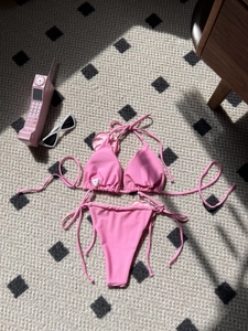 Detailed view of pink string bikini top and bottom with size S tag on flat lay