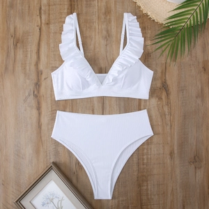 Flat lay of white ribbed V-neck bikini with ruffle shoulder straps on a wood background