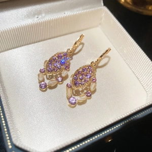 Macro shot of gold earrings with purple stones and oval opal-like inlay in a gift box