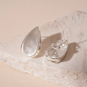Gros plan de boucles d'oreilles larmes argentées avec texture mate et bords polis