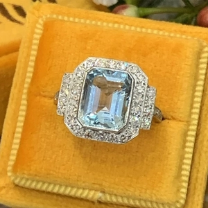 Art Deco emerald-cut light blue zircon ring with halo crystals on yellow velvet box