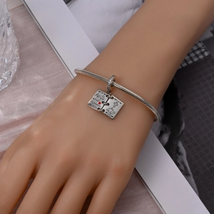 Detail of silver snake chain bracelet with openable 'Peace' book charm on a wrist