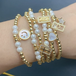 Detail of layered gold beaded bracelet set with shell smiley face and cross charms