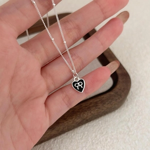 Close-up of heart-shaped silver necklace with black enamel and bow detail held by hand