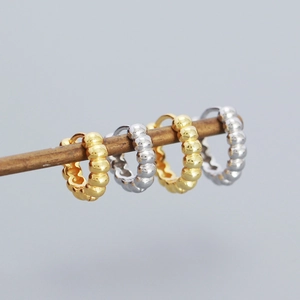 Detailed view of beaded hoop earrings in gold and silver finish hanging on a wood prop