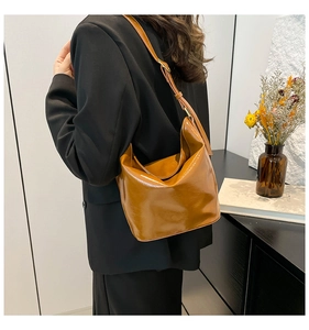 Close-up of caramel leather bucket bag with shiny oil wax finish worn by a model