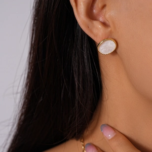 Gros plan sur un élégant clou d'oreille ovale en or avec émail blanc porté par un mannequin