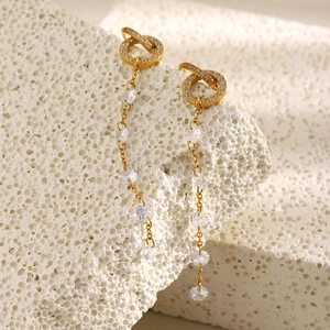 Detail of 18K gold-plated long tassel earrings with clear cubic zirconia on white stone