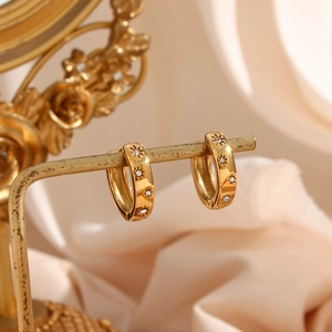 Golden hoop earrings with sunburst pattern and tiny zircon stones on a silk background