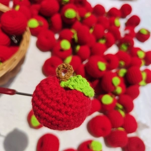 Handmade crochet red apple keychain with green leaf on a knitted wool background