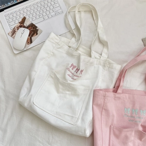 Détail de motifs nœuds brodés et texte sur de grands sacs fourre-tout en toile blanc et rose