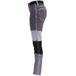 Dettaglio dei jeans patchwork con bordi a taglio vivo e pannelli grigi misti