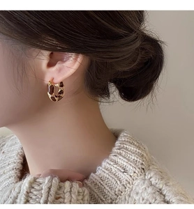 Close-up of golden round hoop earrings with tiger eye stone inlay worn by a model