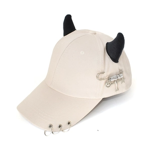 Detail of beige baseball cap featuring black 3D devil horns and silver rings on the brim