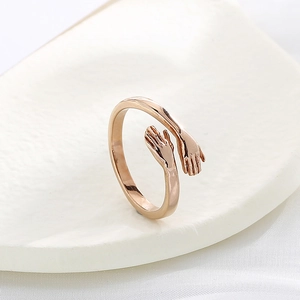 Close-up of rose gold hug ring with hands design on white ceramic display dish