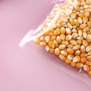 Transparent self-sealing plastic food bag with dried corn kernels on pink background