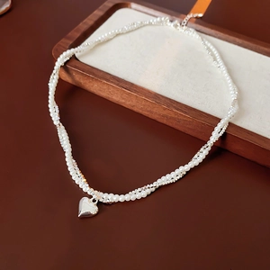 Détail du collier double rang avec cœur, perles blanches et billes argentées sur bois