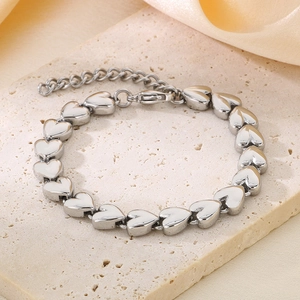 Macro shot of silver heart-shaped chain links on beige stone and pink silk backdrop