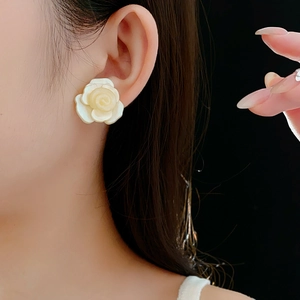 Gros plan d'élégantes boucles d'oreilles roses en résine blanc crème portées