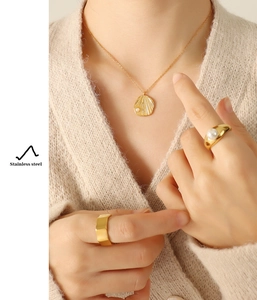 Detail of stainless steel gold pearl necklace and rings worn with a knit sweater