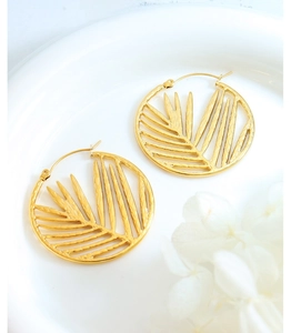 Macro detail of gold bamboo leaf hoop earrings on a minimalist white ceramic tray