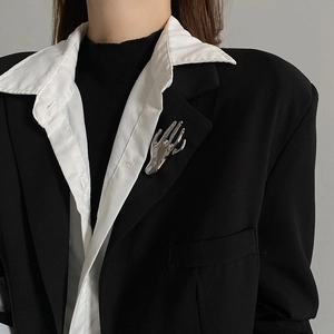 Detailed view of a silver palm-shaped brooch pinned on a black blazer lapel for styling