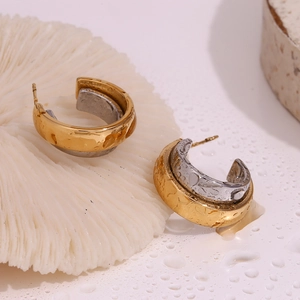 Macro detail of dual-tone gold and silver C-shape earrings on white textured base