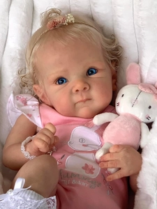 Close-up of Bettie reborn doll with blonde curls, blue eyes, and pink rabbit romper