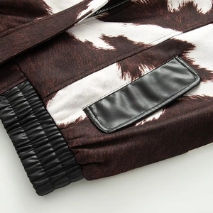 Detail of cow-print plush fabric with black PU leather pocket and ribbed hem on jacket