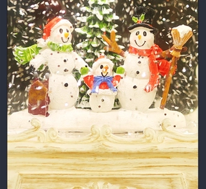Close-up of a festive Christmas snow globe featuring a snowman family and a tree