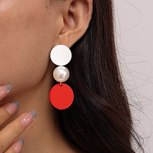 Close-up of geometric asymmetric drop earrings with red and white circles and pearl detail