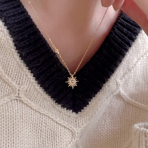 Elegant gold sunburst pendant necklace with zircon stone on a woman wearing a knit sweater