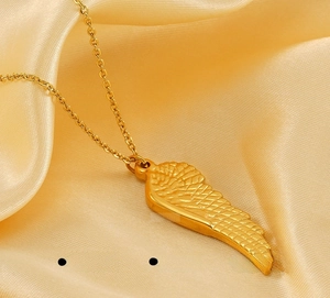 Close-up of polished golden angel wing necklace on soft yellow silk fabric