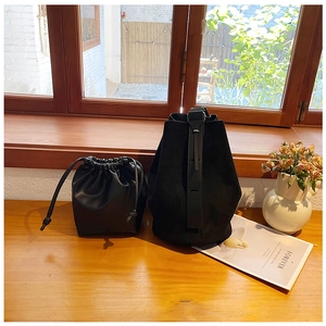Detail of minimalist black suede bucket bag and small leather drawstring pouch on wooden ledge